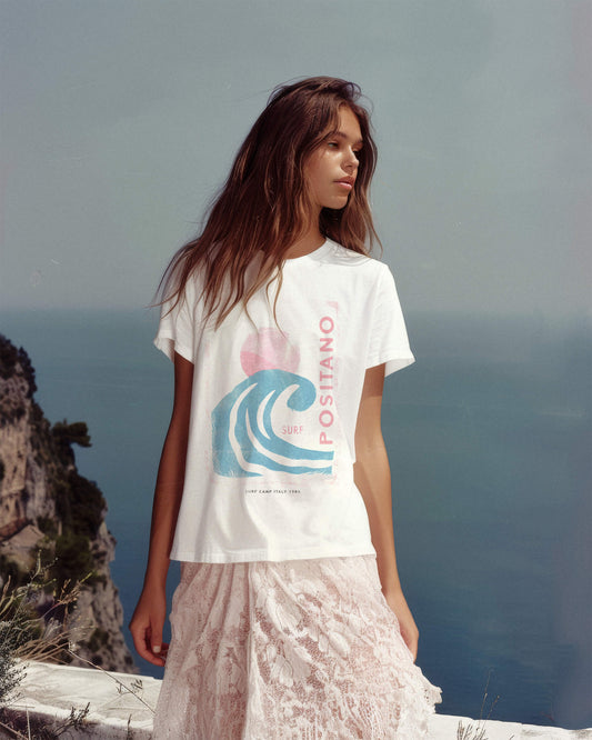 Woman wearing a white t-shirt with a wave design and 'Positano' text, standing on a cliff overlooking the ocean.