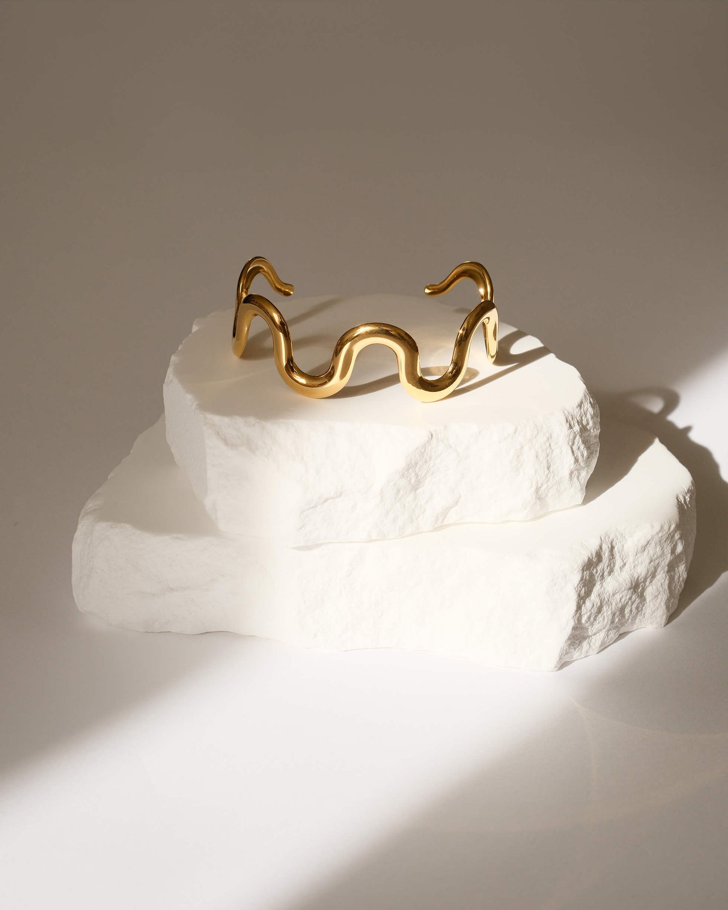 Gold bracelet on a textured white surface with a neutral background